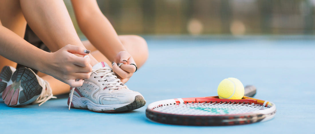 Person tying tennis shoe on a tennis court