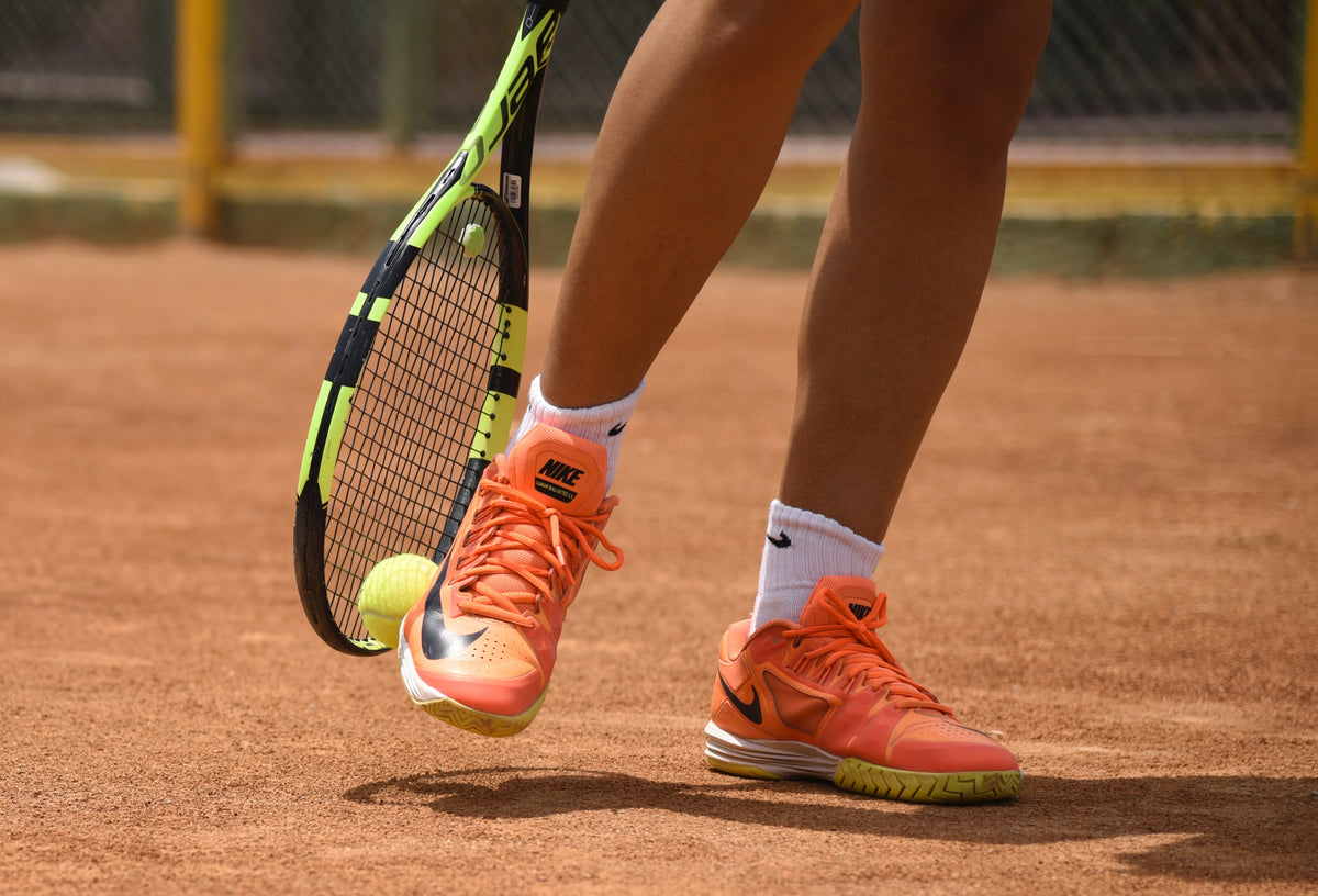 Woman picking ball off ground with tennis racquet and shoe
