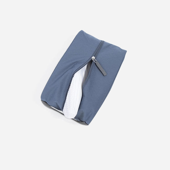 Gray zippered pouch partially open, revealing the sole of a white shoe inside, set against a plain backdrop.