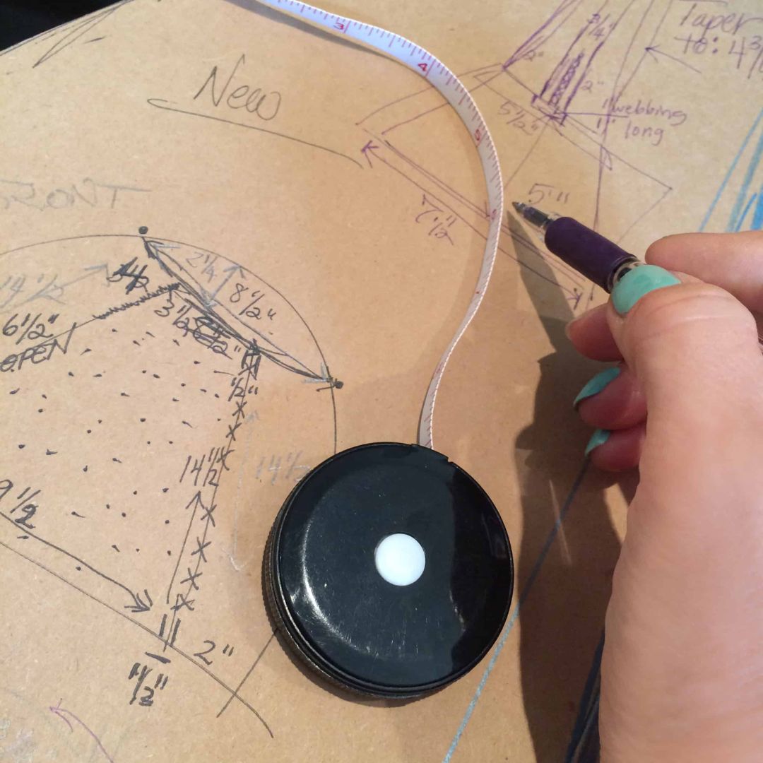 Hand holding a tape measure on a sketch with dimensions and annotations.