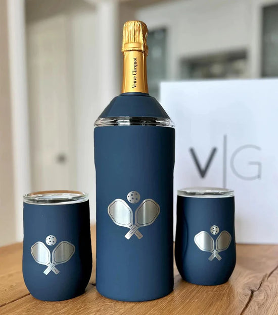 Champagne bottle and two cups with pickleball paddle designs on a wooden surface.