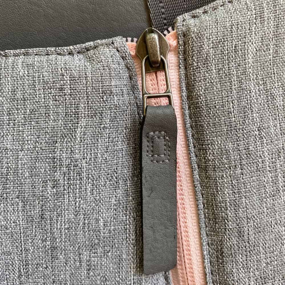 Close-up of a gray fabric bag with a pink zipper and a black leather pull tab.