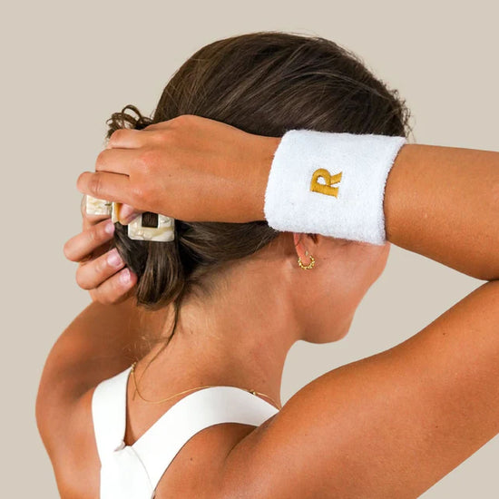 Person with white wristband tying their hair with a clip, wearing a white tank top and hoop earrings.