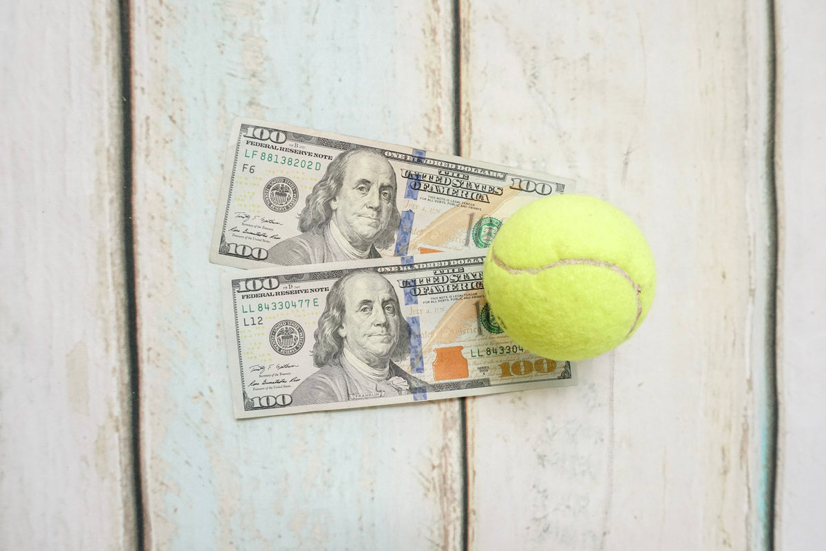 Tennis ball sitting on top of two 100 dollar bills