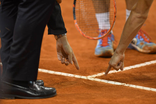 Player and referee pointing at line on clay tennis court