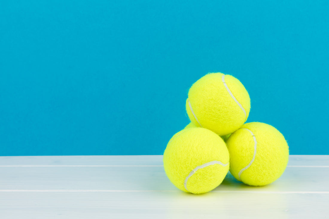 Three tennis balls stacked in front of a turquoise backgournd