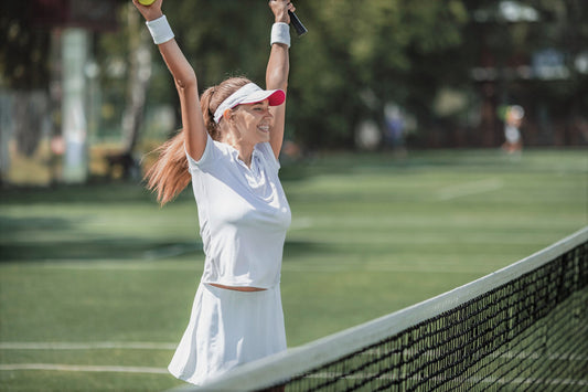 Woman in front of tennis net raising her arms in victory