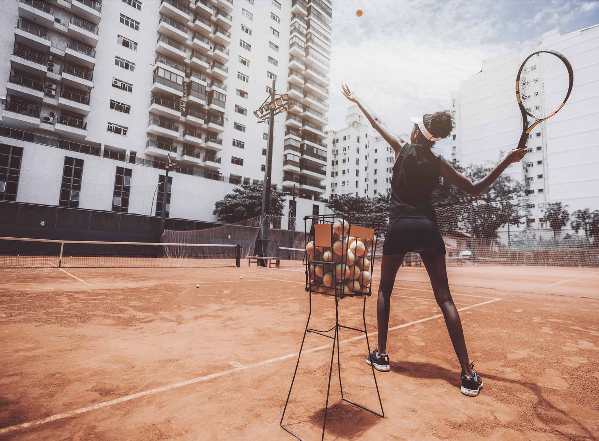 Woman serving from a basket of tennis balls