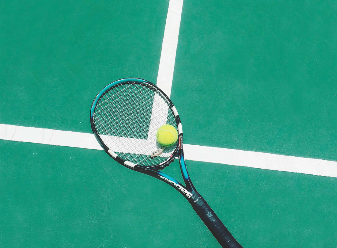 Tennis racquet laying on the tennis court with a ball on top of it