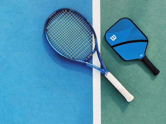 A tennis racquet and a pickleball paddle lying on a court