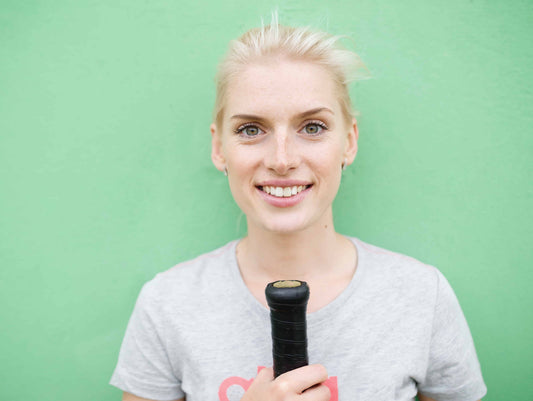 Woman against green background holding tennis racquet upside down