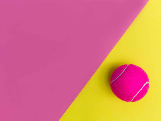 Bright pink tennis ball on yellow part of a pink and yellow background