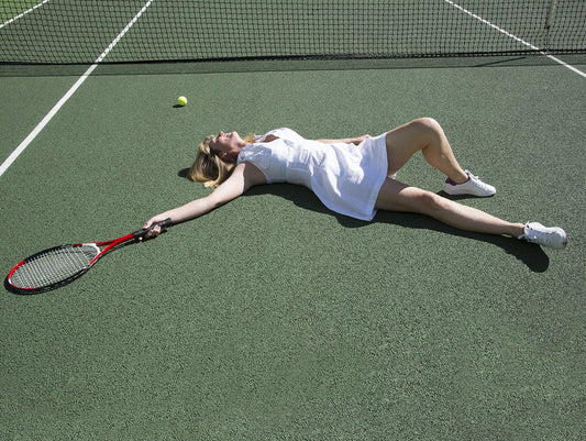 Woman lying on tennis court holding tennis racquet