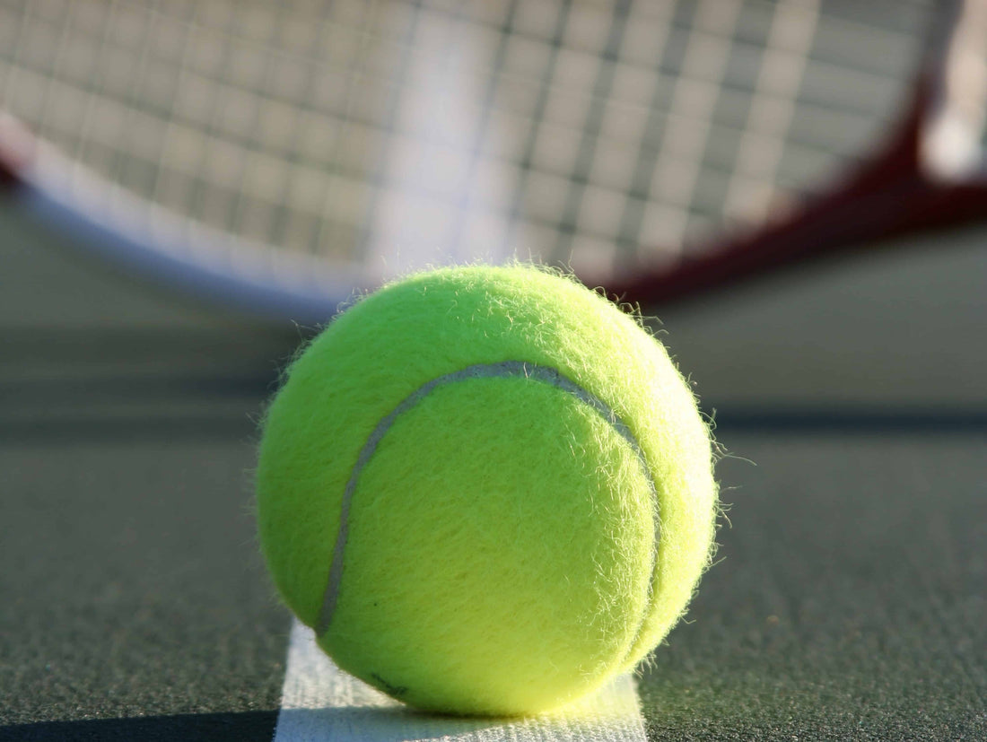 Closeup of tennis ball with racquet in background