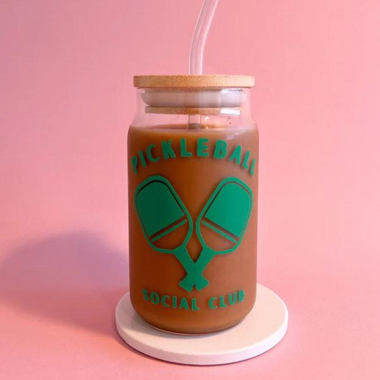 Jar with iced coffee, labeled Pickleball Social Club, on a coaster against a pink background.