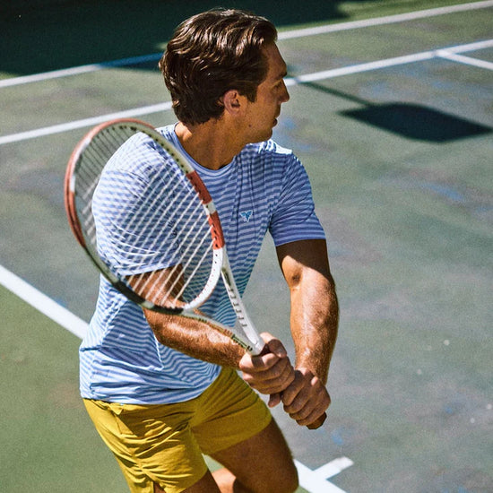 Man playing tennis wearing a stripped tee. 
