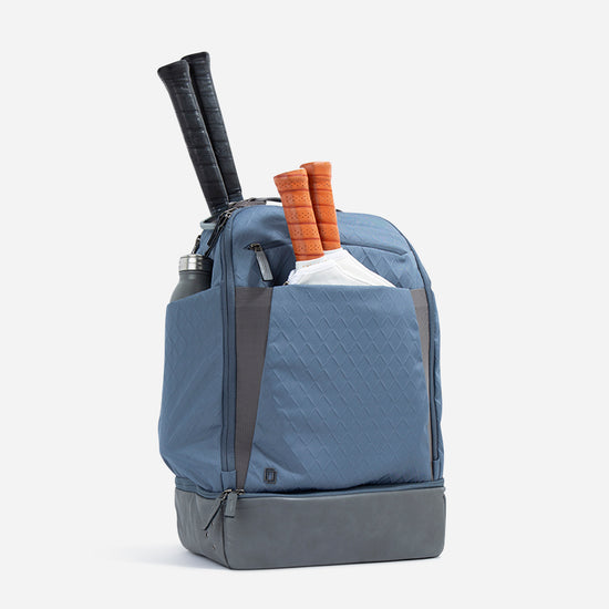 Blue tennis backpack with tennis racquets, water bottle, and a sleek, modern design against a white background.