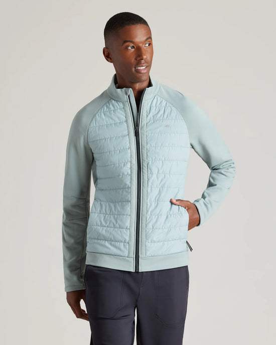 Man wearing a light blue quilted jacket with hands in pockets, looking to the side against a plain background.