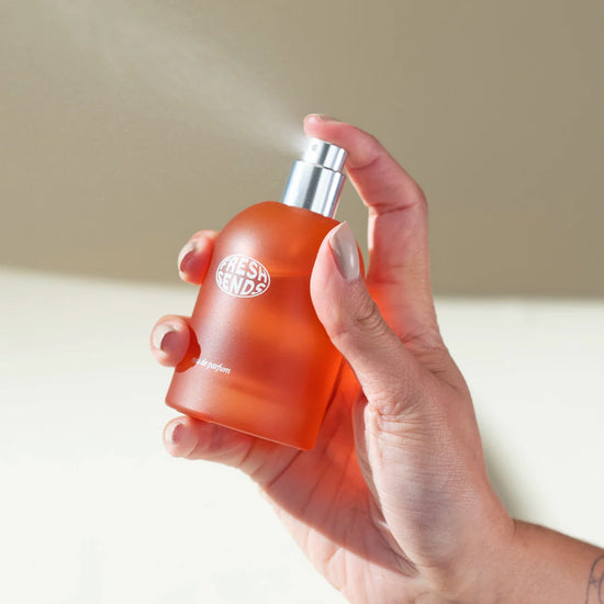 Hand holding an orange spray bottle, releasing fine mist against a light background.