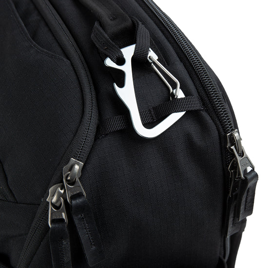 Black tennis backpack with multiple zippers and a silver carabiner clip attached to one of the loops.