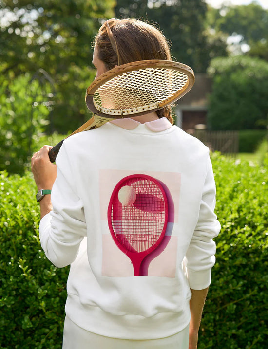 Back of woman wearing a sweatshirt with a tennis racquet and ball print on the back.