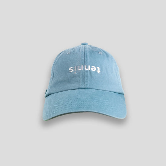 Light blue baseball cap with tennis written upside down in white on the front, set against a gray background.