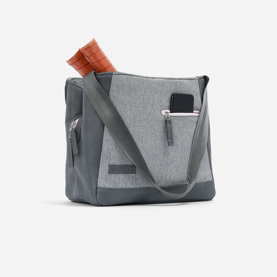 Gray tennis tote bag with leather accents, two handles, a side pocket holding a phone, and rolled papers sticking out on top.
