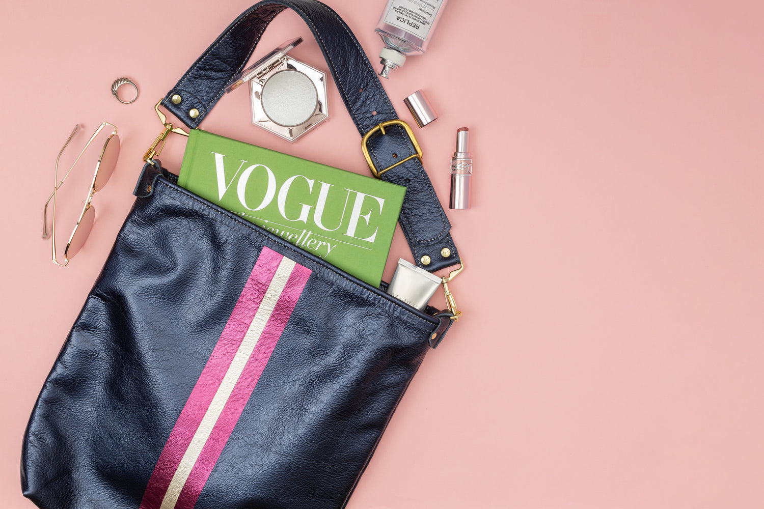 Navy blue leather bag with stripes. Magazine and makeup is spilling out of the bag