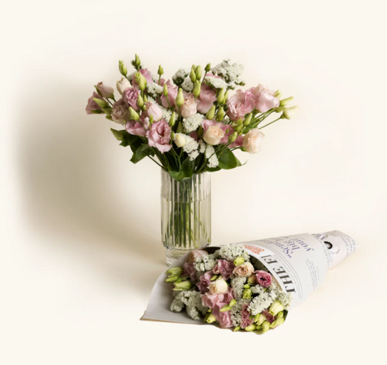Pink and white flowers in a vase with a similar bouquet wrapped in newspaper on a light background.