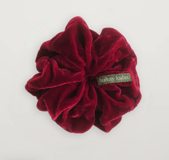 Deep red velvet scrunchie displayed against a soft, neutral background.
