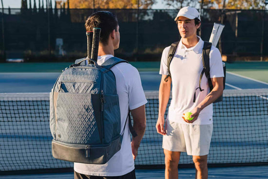 Two men in athletic gear talking on a tennis court, holding racquets and tennis balls.
