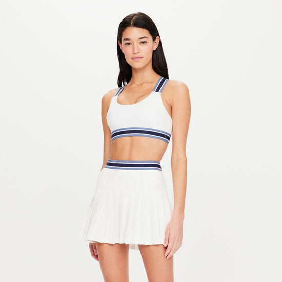 Girl wearing a athletic bra and skirt in white with navy stripe details.