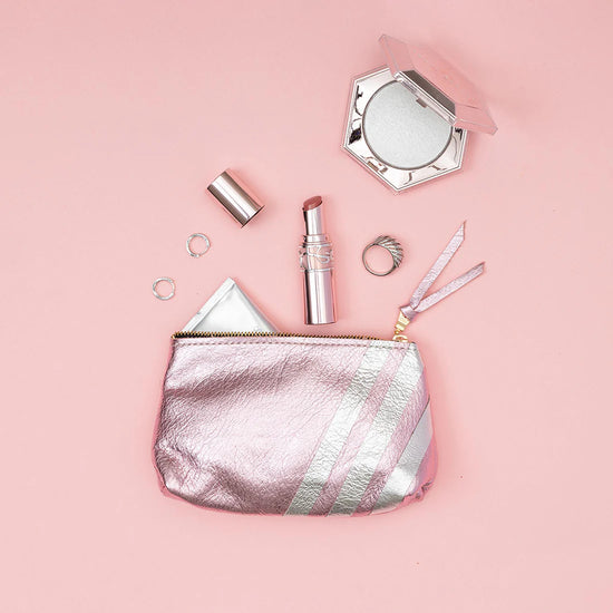 Pink textured pouch with a gold zipper and three diagonal metallic stripes on a pink background.