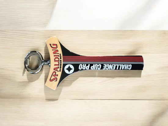 A pickleball paddle with Spalding and Challenge Cup Pro text lies on a light wooden surface.