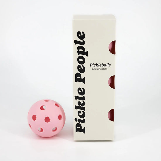 Set of 3 pink pickleballs in a box and one pickleball next to it.